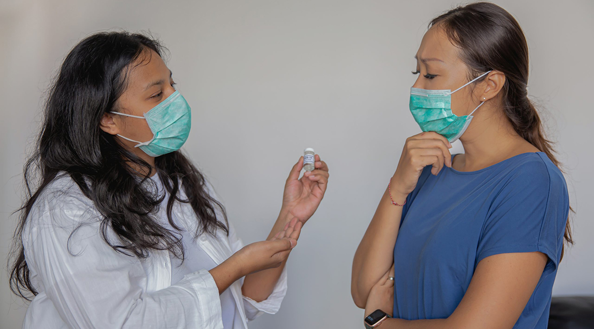 Thoughtful Asian Woman Listening to Healthcare Worker Explaining About Covid-19 Vaccine