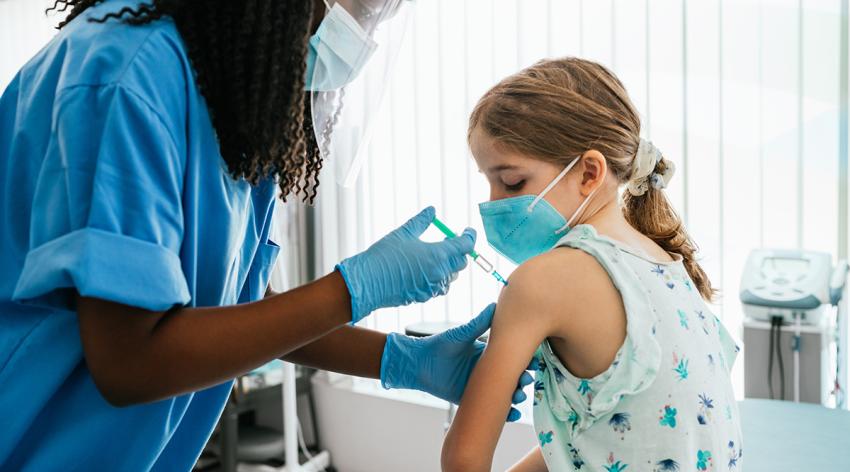 Young girl watching her being injected with COVID-19 vaccine at a medical clinic